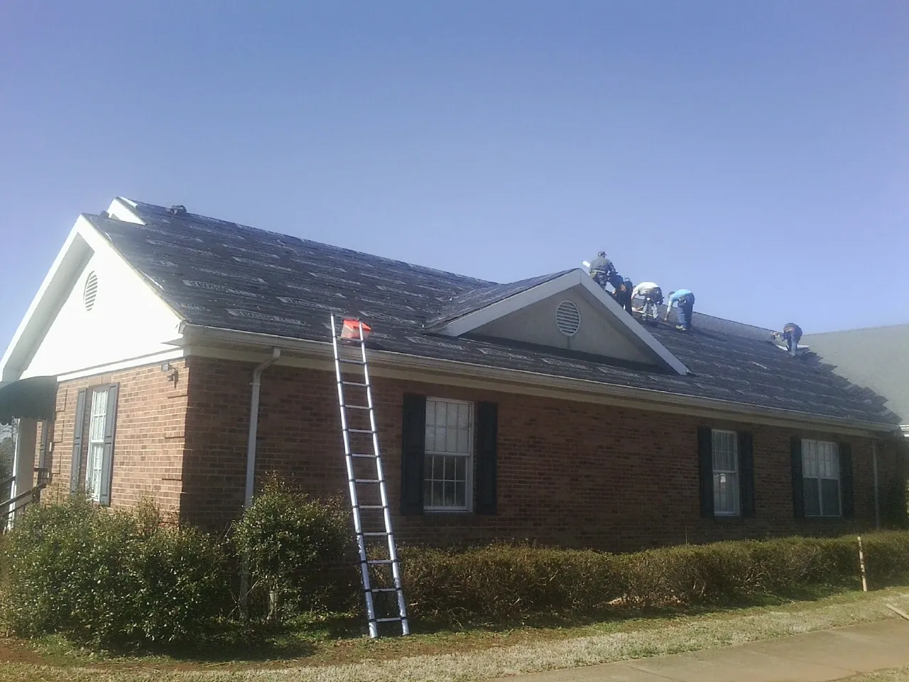 Crew tearing shingles off a brick ranch roof with a ladder set — Metal Roof Repair work by our crew in Catasauqua