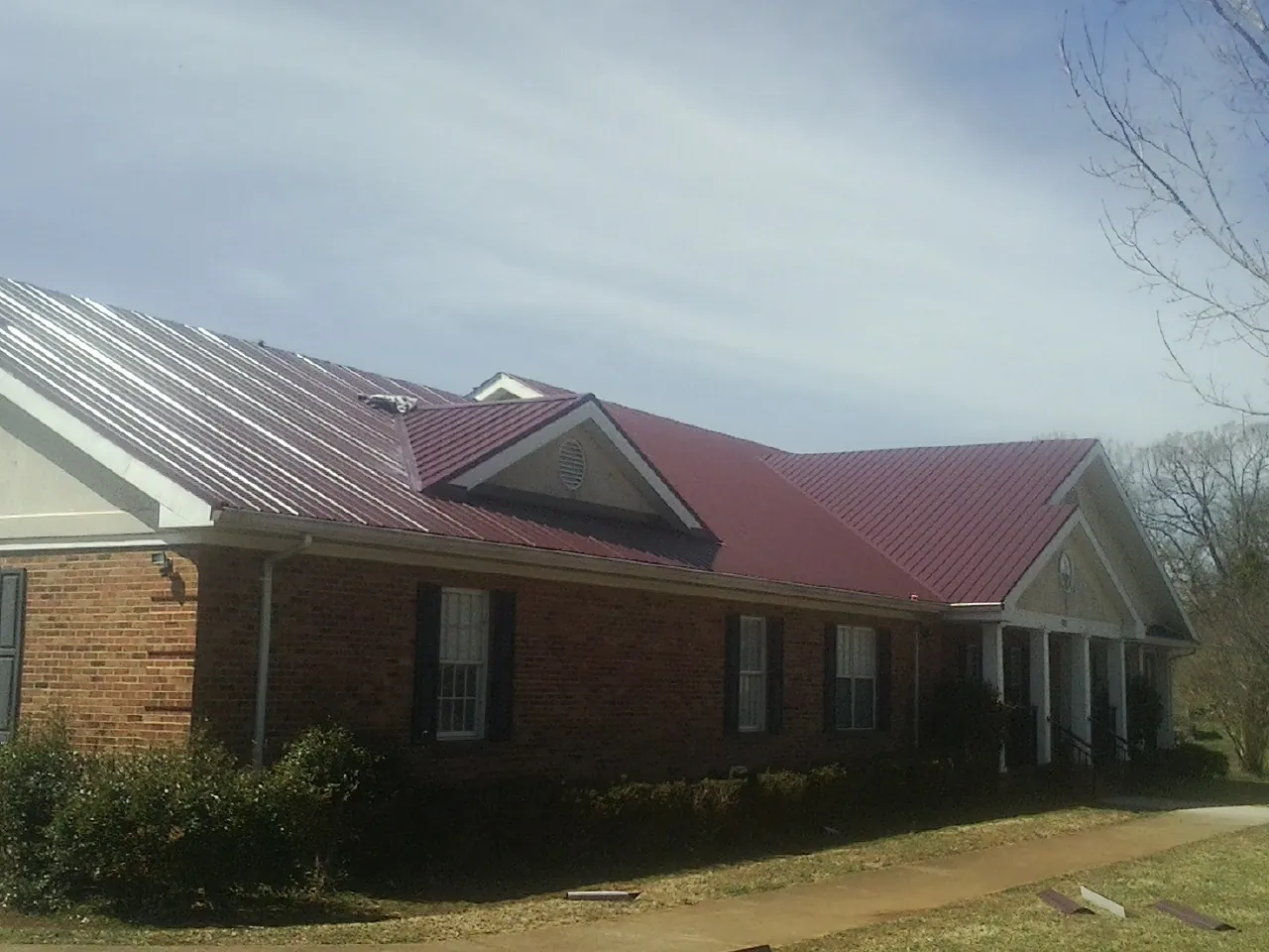 Red metal roof with gabled entries on a long brick building, from a Hail Damage Roof Repair job in Catasauqua