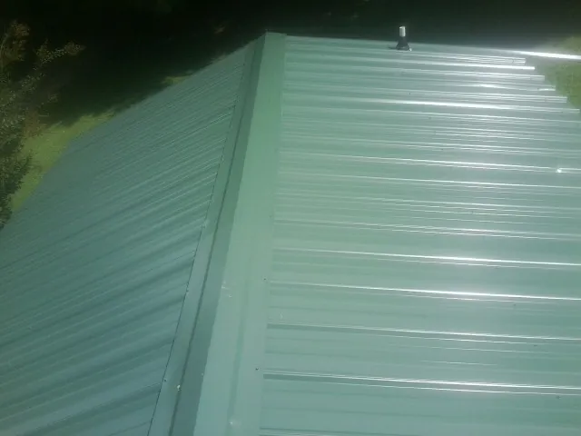 New green metal panels meeting at the ridge of a roof — Flat Roof Repair work by our crew in Catasauqua