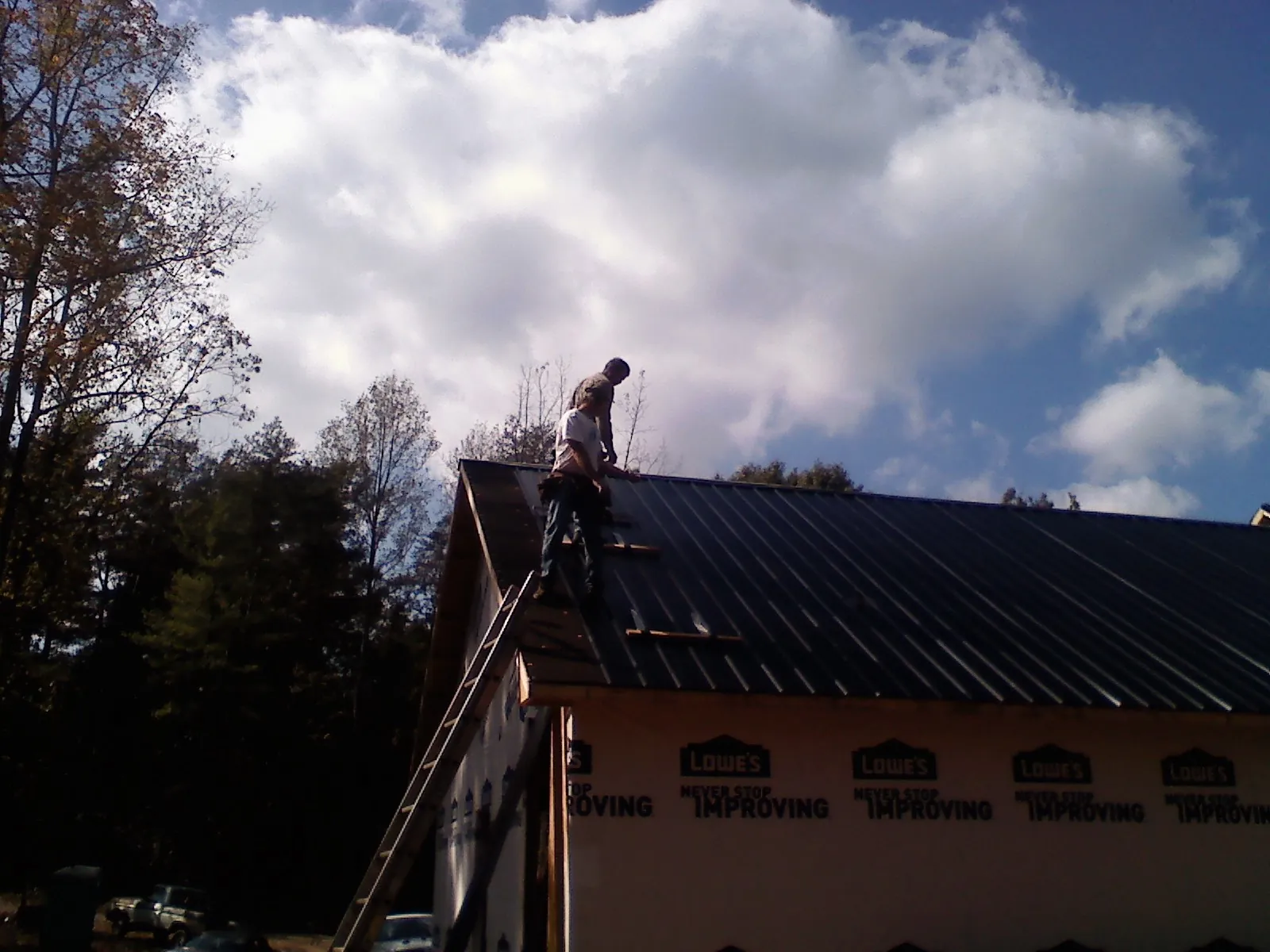 Roofer fastening dark metal panels high against a cloudy sky, from a Roof Inspection job in Catasauqua