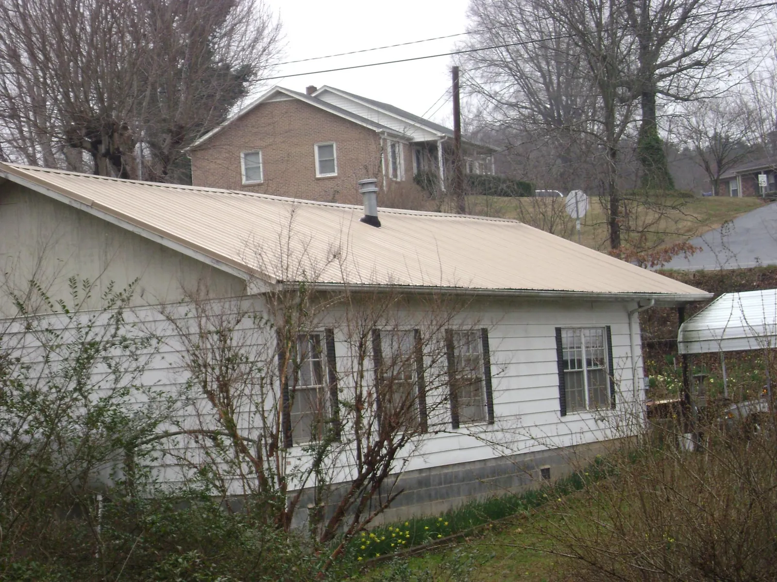 Tan metal roof on a white sided house set into a hillside — Commercial Roofing by Roofing Brothers in Catasauqua